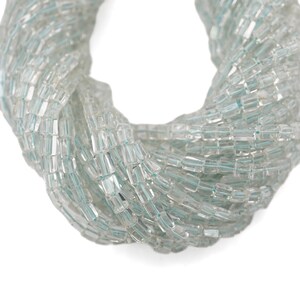 May include: Close-up of a strand of light blue and clear rectangular beads. The beads are strung together, forming a twisted, rope-like shape. The beads have a slightly iridescent quality, reflecting light.