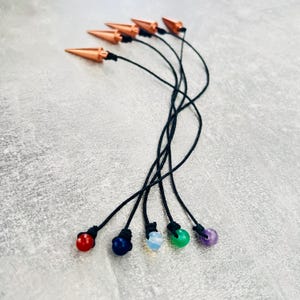 May include: Six copper dowsing rods with black cords and different colored gemstone beads at the end. The beads are red, blue, white, green, and purple.