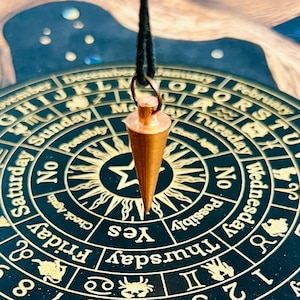 May include: A gold-colored pendulum dangles over a black and gold circular chart with days of the week, zodiac signs, and the words "Yes", "No", and "Possibly" written around the edge.