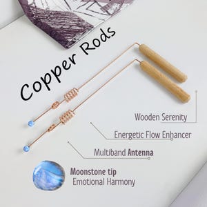 Puede incluir: Dos varillas de cobre con una sección en espiral y una punta de piedra lunar azul. Las varillas están etiquetadas como "Copper Rods" y "Multiband Antenna". Las varillas están acompañadas por dos varillas de madera etiquetadas como "Wooden Serenity" y "Energetic Flow Enhancer".
