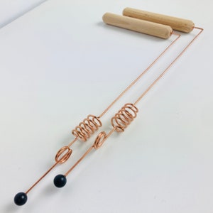 May include: A copper massage tool with two wooden handles and black weighted ends. The tool has two coiled springs.
