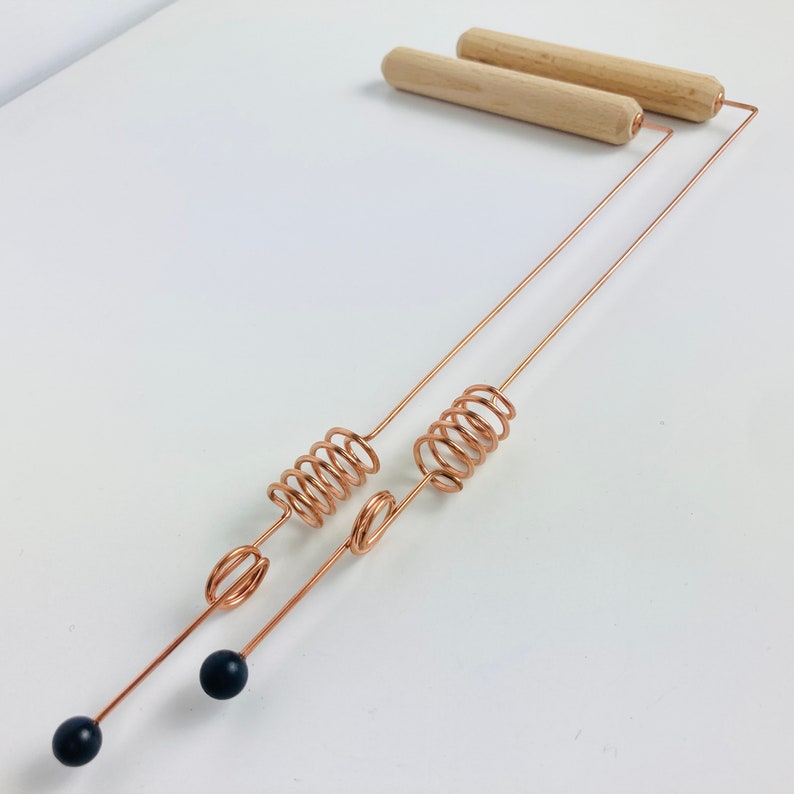 May include: A copper massage tool with two wooden handles and black weighted ends. The tool has two coiled springs.