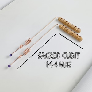 May include: Two copper dowsing rods with wooden handles and purple beads. The rods are labeled "SACRED CUBIT 144 MHZ" in black text. The rods are on a white surface.