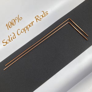 May include: Two 100% solid copper rods, each bent into a 90-degree angle. The rods are on a black surface.