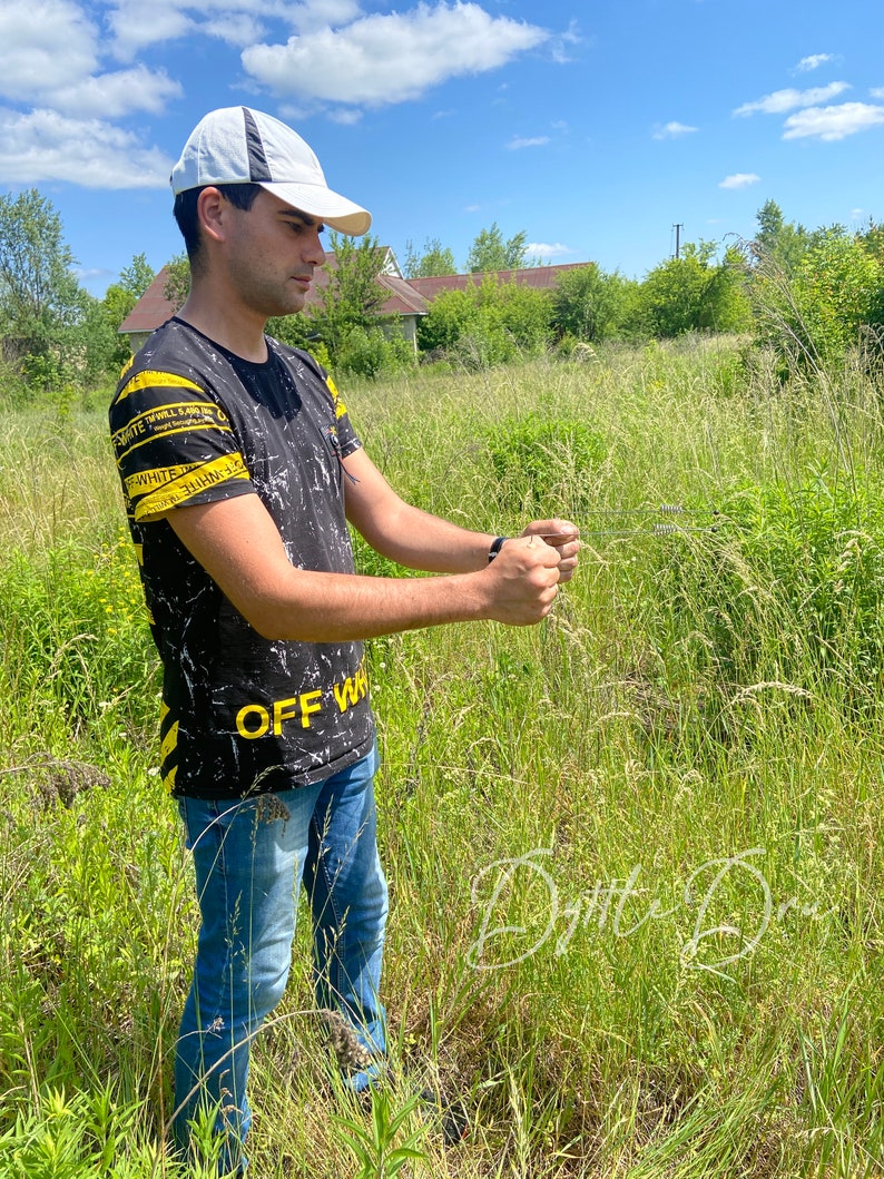 May include: A person wearing a black and white t-shirt with yellow stripes and the text "OFF-WHITE" printed on it. The person is wearing a white baseball cap and blue jeans. The person is standing in a field of tall grass.