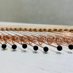 May include: A close-up of a copper wire wall hanging with black beads. The wire is coiled into a spiral shape and the beads are evenly spaced along the wire.