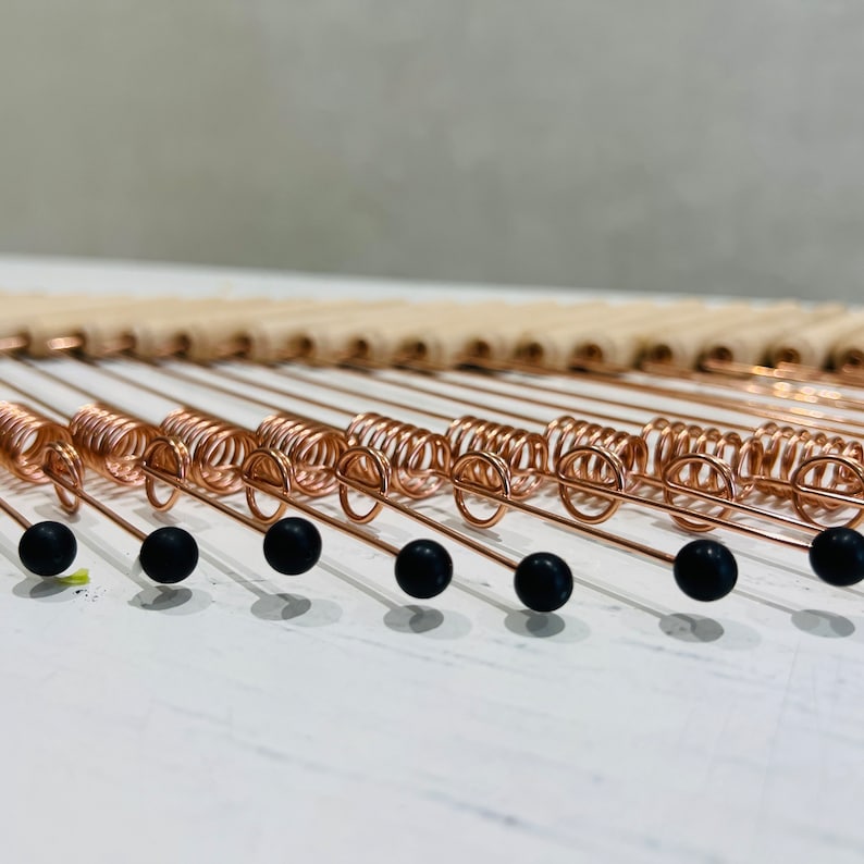 May include: A close-up of a copper wire wall hanging with black beads. The wire is coiled into a spiral shape and the beads are evenly spaced along the wire.
