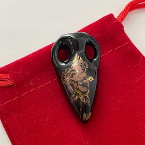 May include: Black ceramic pendant shaped like a bird's head with a gold and pink rose design.
