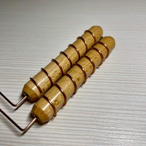 May include: Two wooden tools with copper wire wrapped around the handles. The wooden handles are cylindrical and light brown. The copper wire is wrapped in a spiral pattern. The tools have a metal wire extending from the base.