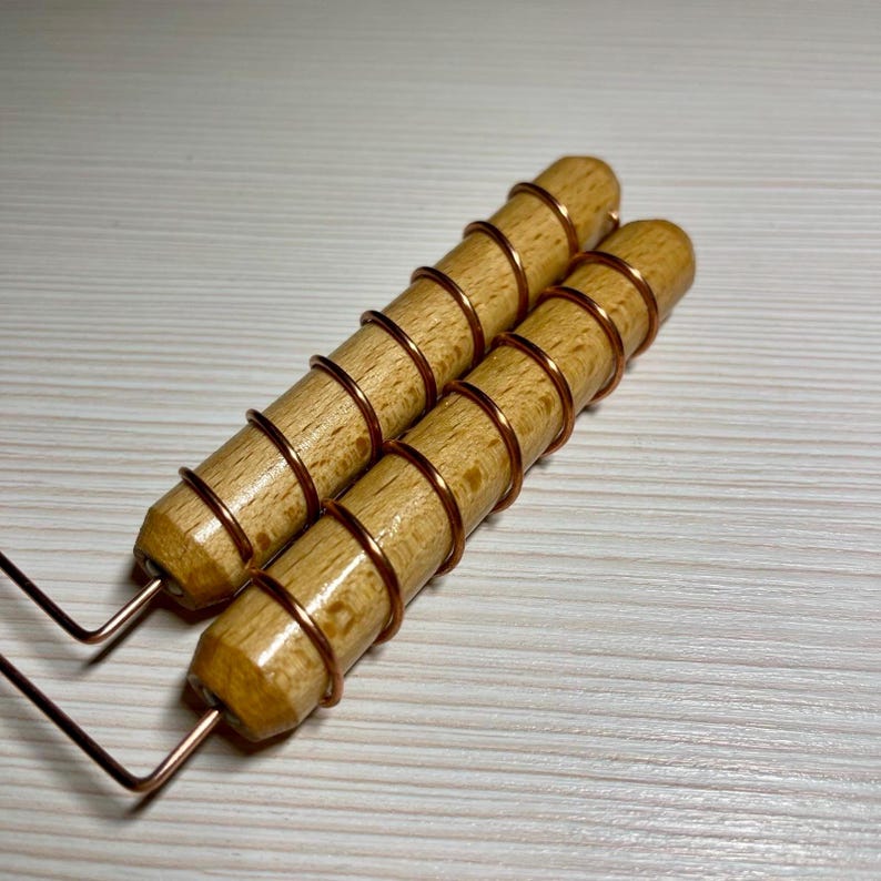 May include: Two wooden tools with copper wire wrapped around the handles. The wooden handles are cylindrical and light brown. The copper wire is wrapped in a spiral pattern. The tools have a metal wire extending from the base.