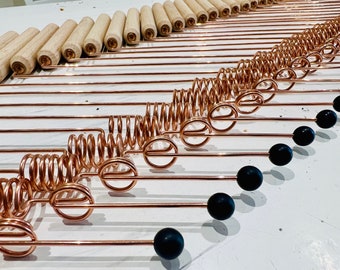 May include: A set of copper-colored metal rods with a spring and a black ball on the end. The rods are arranged in a diagonal line.