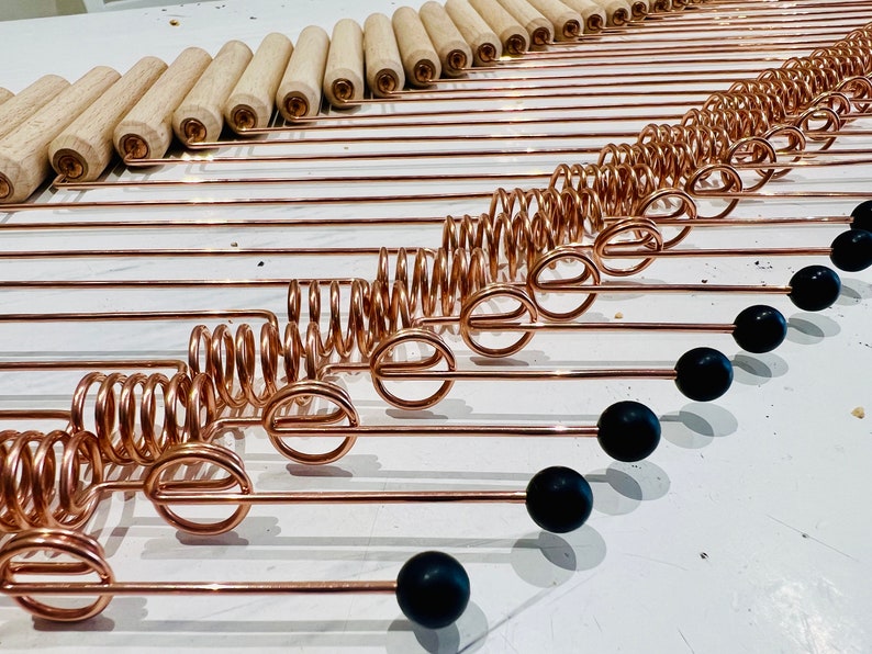 May include: A set of copper-colored metal rods with a spring and a black ball on the end. The rods are arranged in a diagonal line.