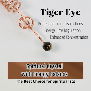 May include: A copper-colored wire wrapped into a spiral and a loop, with a small, round tiger eye stone at the end. Text reads "Tiger Eye" and describes benefits like "Protection from Distractions".