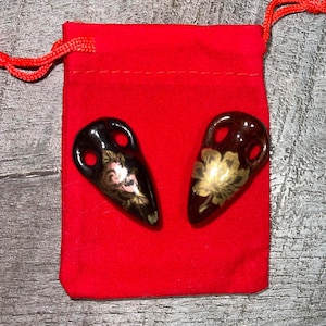 Puede incluir: Dos pequeñas figuritas de cerámica marrón oscuro con diseños florales dorados y rosados. Las figuritas están sentadas sobre una bolsa de terciopelo rojo.