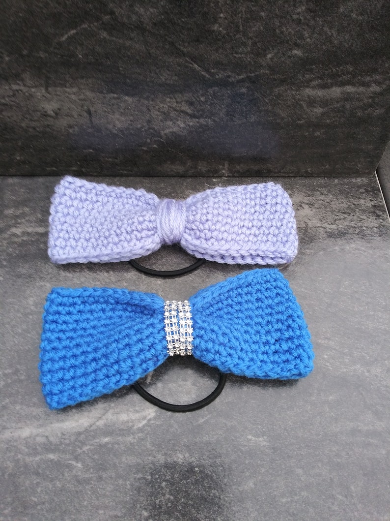 May include: Two knitted hair ties, one light purple and one blue, with a rhinestone embellishment on the blue hair tie.