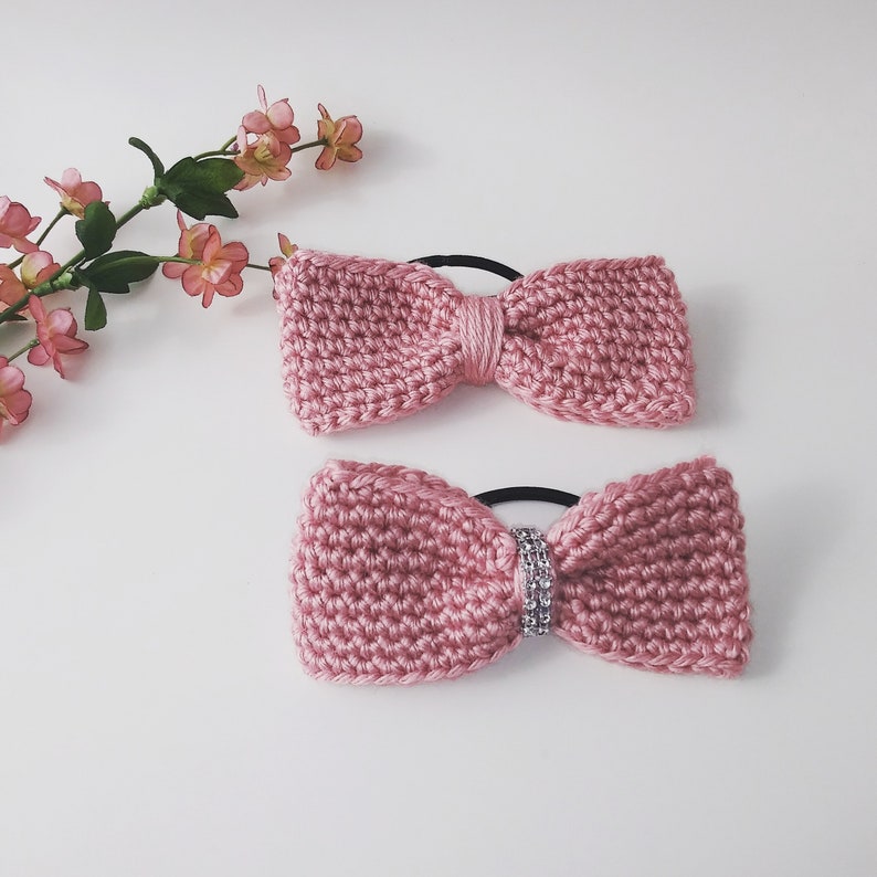 May include: Two pink crocheted hair bows with elastic bands. One bow has a rhinestone embellishment.