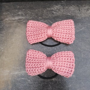 May include: Two pink crocheted hair scrunchies with black elastic bands.