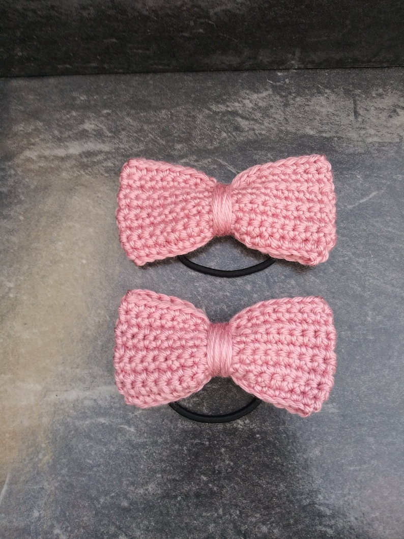 May include: Two pink crocheted hair scrunchies with black elastic bands.