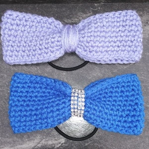 May include: Two crocheted hair ties, one in lavender and one in blue. The blue hair tie has a rhinestone embellishment in the center.