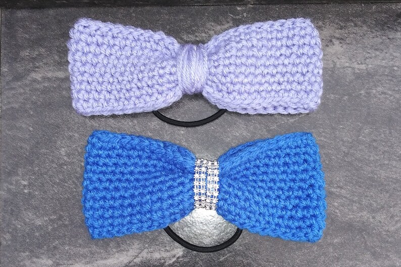 May include: Two crocheted hair ties, one in lavender and one in blue. The blue hair tie has a rhinestone embellishment in the center.