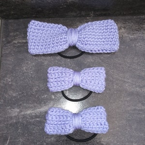 May include: Three purple knitted hair scrunchies in different sizes. The scrunchies are tied in a bow shape.