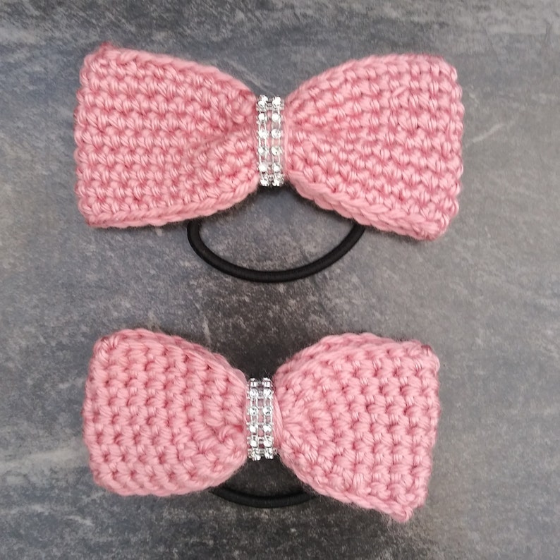 May include: Two pink crocheted hair scrunchies with a rhinestone embellishment.
