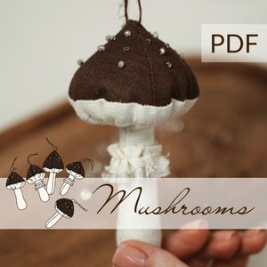 May include: A brown and white fabric mushroom ornament with a string for hanging. The mushroom is decorated with silver beads. The text "Mushrooms" and "PDF" are visible in the image.