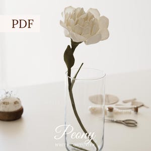 May include: A white fabric peony flower with a dark green stem and leaves placed inside a clear glass cylindrical vase. The image includes the text PDF, Peony, WHITE COUTURIER, and ENG-UA-RU. Crafting supplies are visible in the background.
