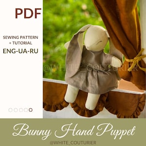 Puede incluir: Una marioneta de mano de conejo hecha a mano con tela beige y marrón, con un vestido marrón. La imagen incluye texto que dice "PDF", "SEWING PATTERN + TUTORIAL" y "Bunny Hand Puppet". El fondo es verde borroso.