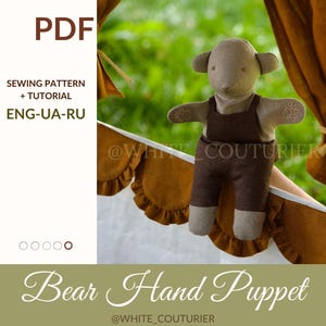 May include: A beige bear hand puppet with brown overalls. The image includes text that says "PDF", "SEWING PATTERN + TUTORIAL", and "Bear Hand Puppet". The puppet is set against a backdrop of green foliage and brown fabric.