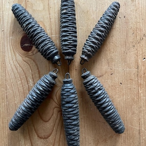 May include: Six dark brown wooden pine cone shaped ornaments with a metal loop at the top.