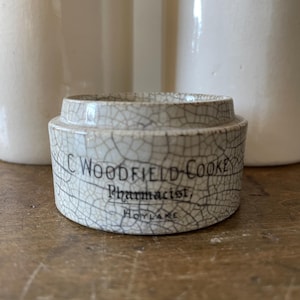 May include: White ceramic jar with a crackled glaze. The jar has a label that reads "C. Woodfield Cooke, Pharmacist, Hoylake".