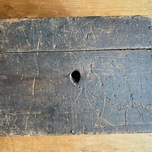 May include: A dark brown wooden box with a single hole in the top. The box is made of rough-hewn wood and has a worn, rustic appearance.