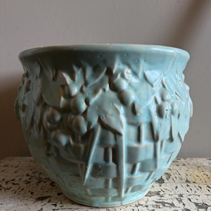 Pode incluir: Um vaso de cerâmica turquesa com um design de tecido de cesta e detalhes em relevo de uvas e folhas. O vaso redondo tem uma abertura larga e é adequado para uso interno ou externo.