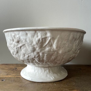 May include: White ceramic bowl with a raised leaf design. The bowl has a pedestal base.