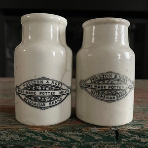 May include: Two white ceramic jars with black lettering. The jars are labeled "POULTON & NOEL HOME-MADE POTTED MEATS BELGRAVIAN BRAND".