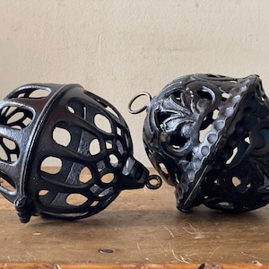 Pode incluir: Dois ornamentos decorativos em forma de gaiola de ferro fundido preto. Um ornamento tem um design circular e o outro tem um design floral mais intrincado.