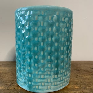 May include: A teal blue ceramic vase with a textured woven pattern.