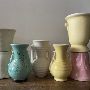 May include: Five vintage ceramic vases in various colors and styles. The vases are arranged in a row on a wooden surface. The vases are all different sizes and shapes, and they have a variety of decorative details.