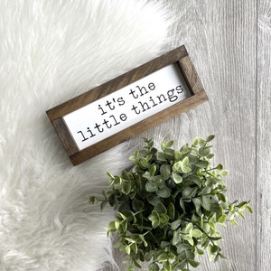 May include: A handmade wooden sign displaying the word "Welcome" in a playful font. The white-painted sign has a distressed finish and a floral design in pinks and greens. It measures approximately 30 cm wide and 15 cm tall.