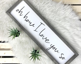 May include: A white wooden sign with a gray frame, featuring the text "oh how I love you so" written in black cursive script.