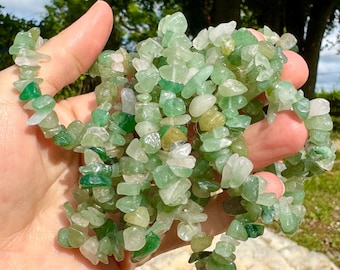 May include: A handful of green aventurine chip beads. The beads are a mix of light and dark green, with some translucent and opaque pieces. The beads are strung together, forming a necklace or bracelet.