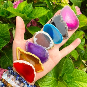 Puede incluir: Una colección de siete rebanadas de ágata en varios colores, incluyendo rojo, naranja, amarillo, morado, azul, marrón y rosa. Las rebanadas están dispuestas en un patrón de arcoíris y se sostienen en una mano.