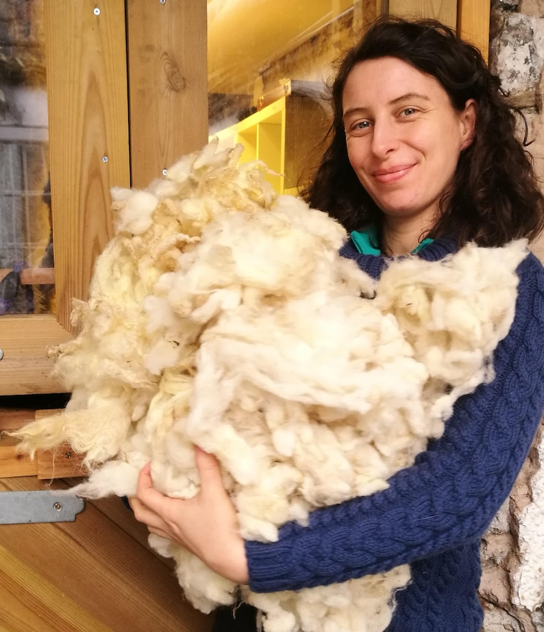 May include: A large pile of white sheep wool being held by a person. The wool is fluffy and soft, and the person is smiling.