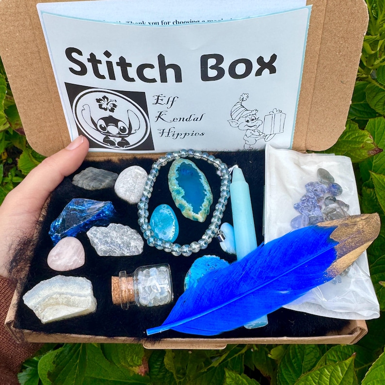 May include: A Stitch Box with various items, including crystals, a bracelet, a blue feather, and a candle. The box has a black interior and a Stitch character logo. The text "Elf Kendal Hippies" is also visible.