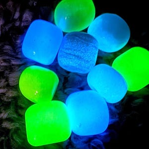 Könnte beinhalten: Eine Ansammlung leuchtender, abgerundeter Steine in Blau- und Grüntönen. Die Steine haben eine glatte Textur und strahlen ein helles Neonlicht vor einem dunklen Hintergrund aus. Die Anordnung deutet auf einen dekorativen oder handwerklichen Gegenstand hin.