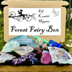 May include: A cardboard box filled with various crystals and stones. The box is labeled "Forest Fairy Box" and has a logo with a fairy and the text "Elf Kendal Hippies".