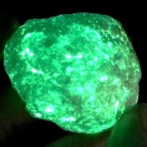 May include: A large, green, translucent rock that glows under a black light. The rock has a rough, uneven surface and is irregularly shaped.