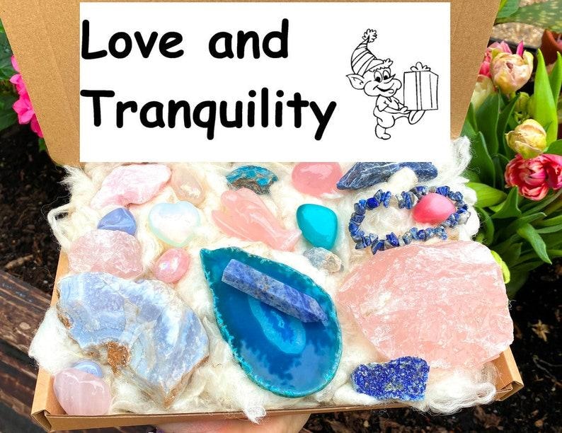 May include: A box filled with various pink, blue, and white crystals and stones. The box is labeled "Love and Tranquility".