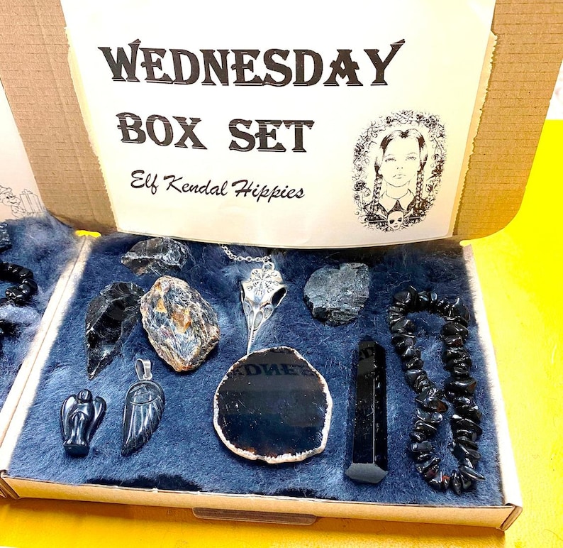May include: A box set with the text "WEDNESDAY BOX SET Elf Kendal Hippies" on the lid. The box contains a variety of black crystals, a silver pendant, and a black beaded bracelet.